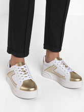White sneakers with gold accents worn by a person on a white background